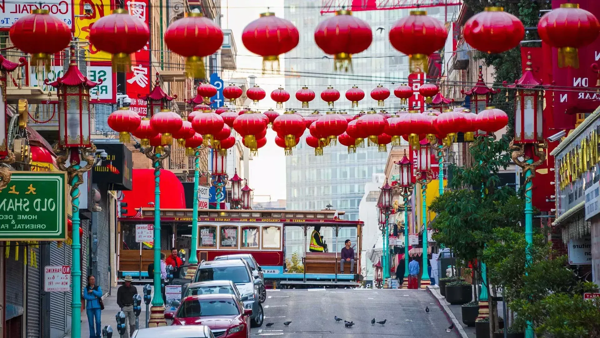 A hilly street in San Francisco's Chinatown is pictured with red lanterns dangling and a streetcar passing by.