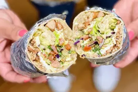 A mission-style burrito, wrapped in foil and cut in half, is shown to the camera.